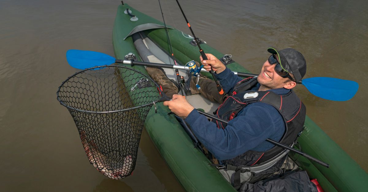 Man holding up a fish in a net that he caught on a river bank