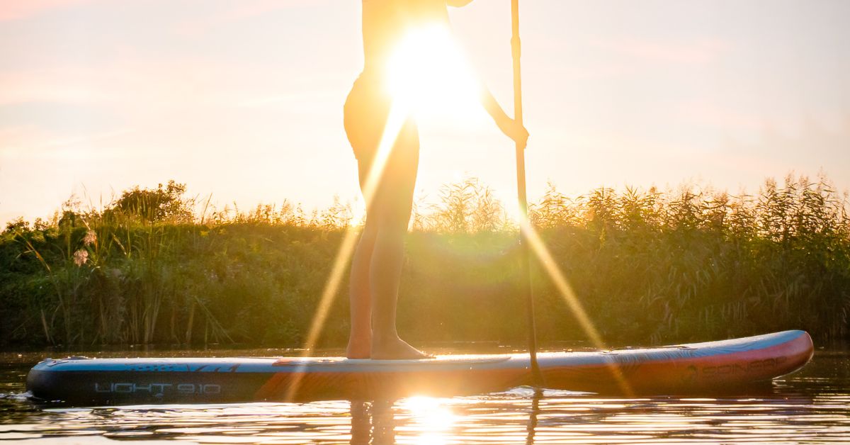 Man on standing on a paddle board with the sun setting in the background